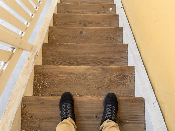 Person standing on old wooden staircase with dirty steps, seeing personal perspective