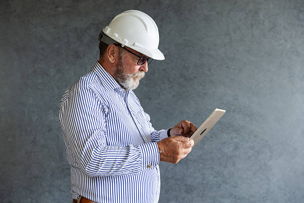 istock An older engineer wearing a white safety helmet uses a digital tablet, symbolizing modern construction practices, technology integration, and innovation in engineering and architectural project management. 2236841444