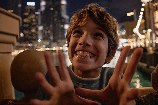 Young boy smiling with hands raised, experiencing joy and wonder with blurred city lights