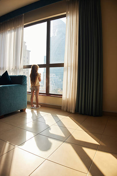 istock Child looking out apartment window at city view 2236843924