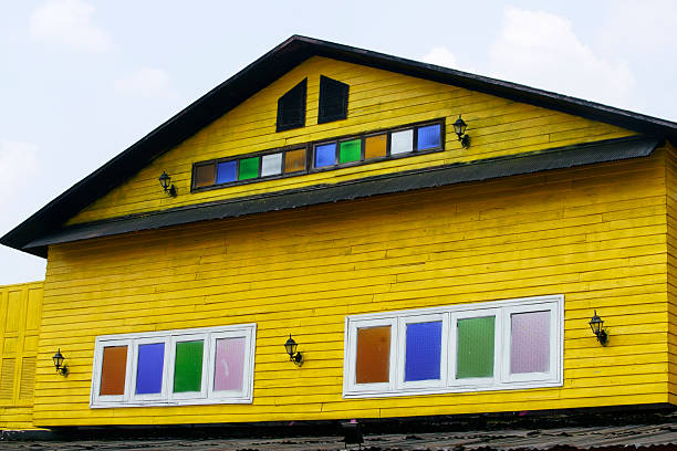 A stunning yellow house featuring colorful windows creates a cheerful ambiance. The design stands out against a bright sky, showcasing vibrant architecture.