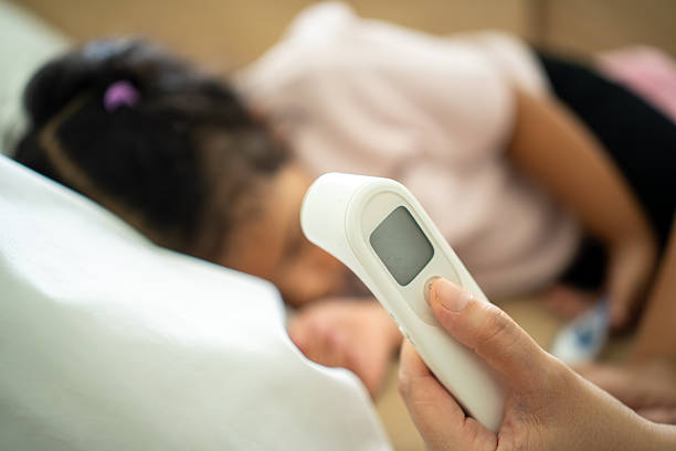 istock Vertical selective focus at woman hand holding digital infrared thermometer checking temperature of sick child’s fever lying on bed, child health insurance and family medical coverage concept. 2236845109
