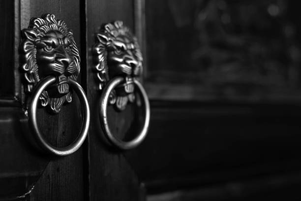 A pair of ornate lion-shaped metal door knockers on dark wooden doors, captured in black and white.