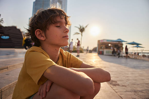 Boy sitting with eyes closed enjoying a peaceful moment by the water at sunset