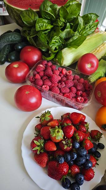 istock Fresh summer fruits and vegetables arranged on a white table, including strawberries, tomatoes, raspberries and herbs 2236847639