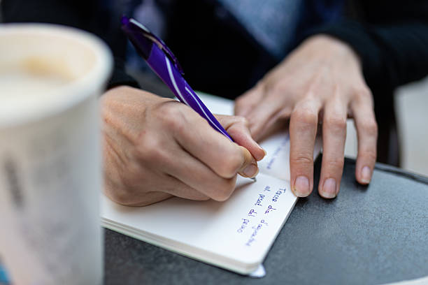 istock Close up of hands writing notes in notepad with purple pen, with blurred disposable coffee cup in background, in marrakech 2236850834