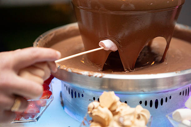 istock Hands dipping marshmallow on a stick into a chocolate fountain 2236852760