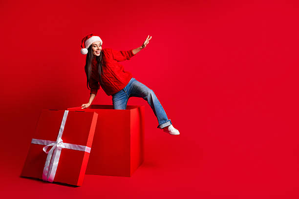 istock Exciting holidays with a woman posing joyfully inside a large red gift box wearing festive santa outfit 2236853330