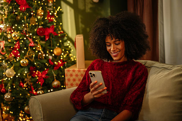 istock Young woman using phone, sitting next to Christmas tree 2236853738