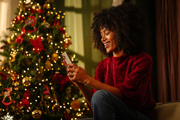 istock Young woman using phone near christmas tree at home 2236853748