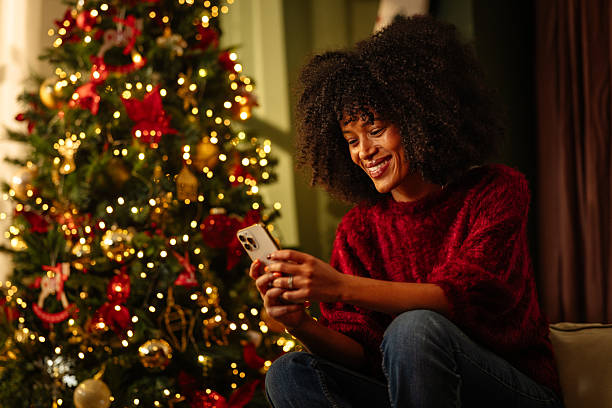 istock Young woman using smartphone near illuminated Christmas tree at home 2236853755