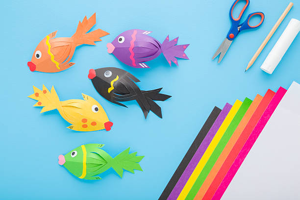 istock Fishes, scissors, glue stick, pencil and colorful application paper on light blue table background. Pastel color. Closeup. Child created shapes. Top down view. 2236854184
