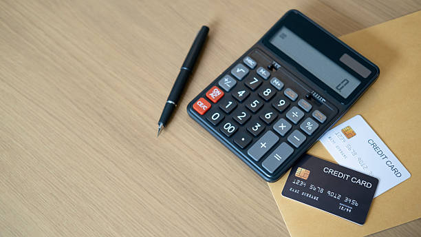 istock A black calculator displaying zero sits on a wooden surface next to a brown envelope with black and white credit cards while a fountain pen lies nearby reflecting finance calculation control and household security. 2236854907