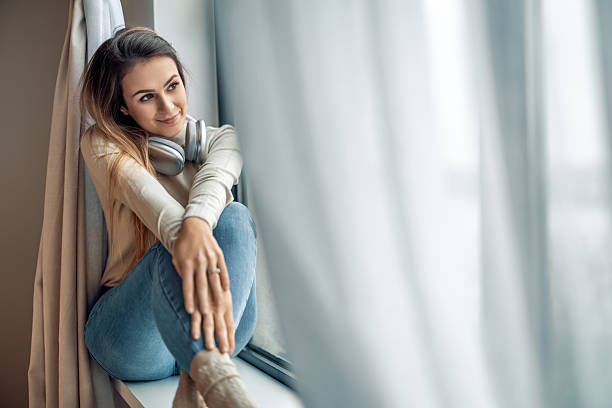istock Woman sitting by the window smiling and enjoying music while wrapped in soft natural light at home 2236856442