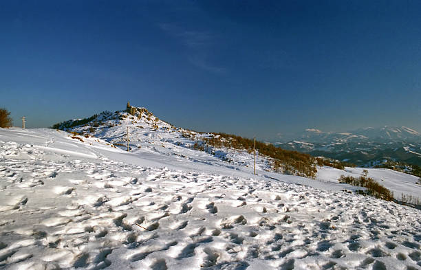 numerous footprints of people on a snow-covered field against a clear sky