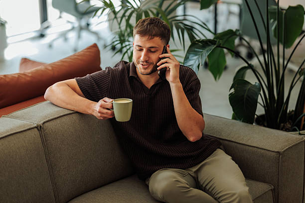 istock Young man talking on phone, drinking coffee in office lounge 2236867954