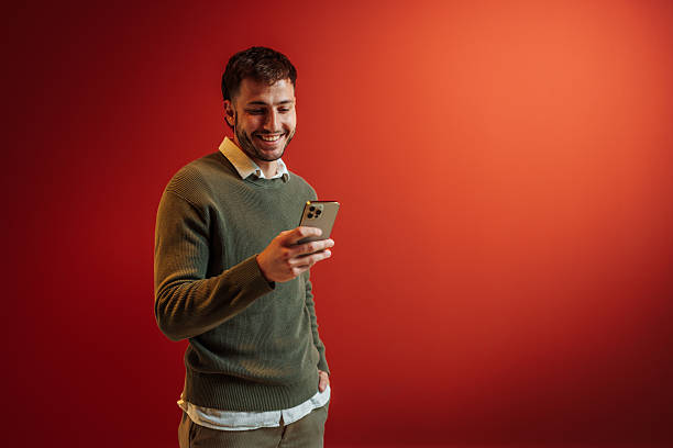 istock Young adult smiling using smartphone with red background 2236868024