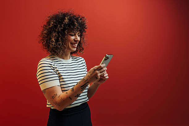 istock Happy young woman checking smart phone against red background 2236868144