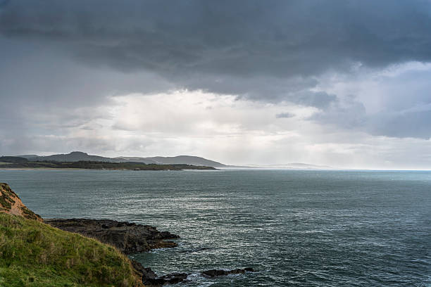 Dramatic Irish coastline with rocky cliffs, grassy slopes, stormy sea and clouds, horizontal landscape, no people.