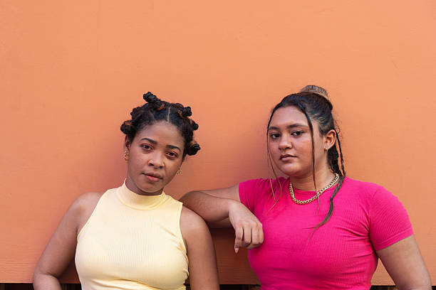 Young women leaning on an orange wall, expressing confidence and diverse style