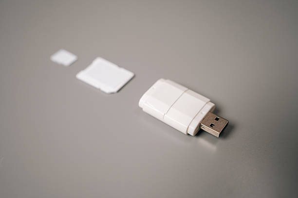 istock Close-up of white micro sd card reader featuring usb connector resting on gray table, accompanied by adapter and microSD card, highlighting compact 2236880682
