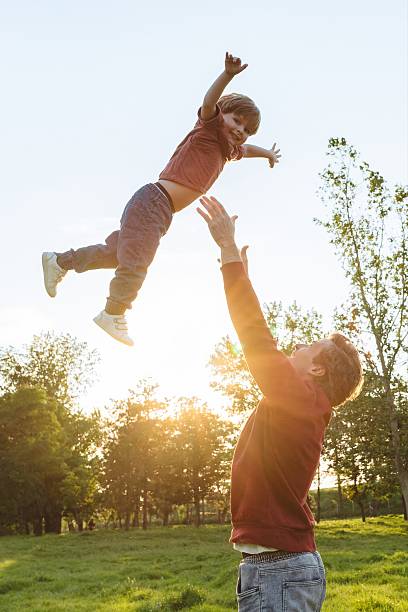 istock Father tossing his joyful son into the air in a park 2236881082