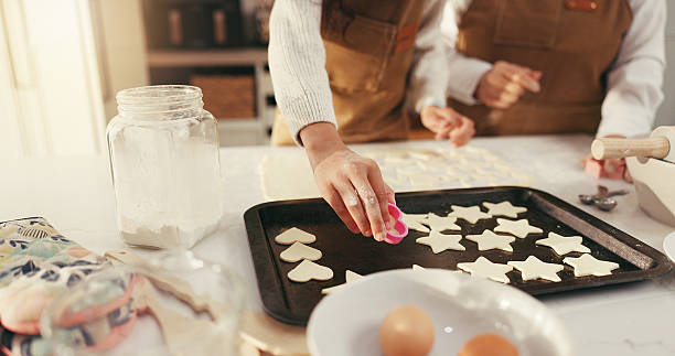istock Baking, hands and biscuits on tray in kitchen for teaching, bonding or fun activity together in home. Learning, cooking and people preparing dessert or cookies on counter for development in house. 2236881302