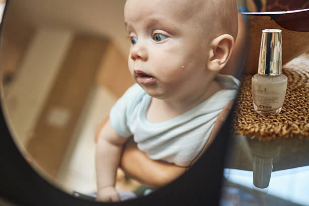 A baby boy lies on his change pad looking at his reflection in a round mirror.