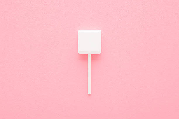 White square shape lollipop on stick on light pink table background. Pastel color. Sweet candy. Closeup. Top down view.