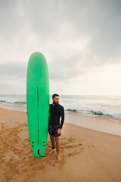 istock Young handsome male surfer with a surfboard is enjoying a view while walking a sandy beach at sea. Summer, vacation, ocean 2236893531