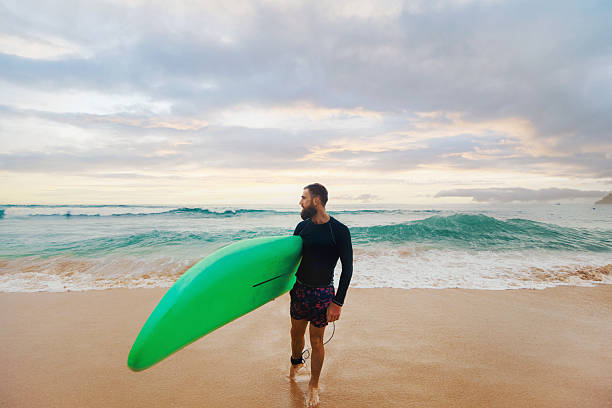istock Young  bearded man with surfboard standing near a beach. Man with surfing board outdoors on a summer day. 2236893541