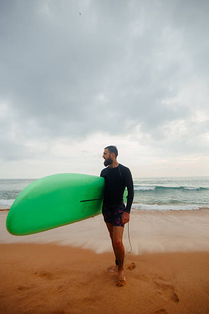 istock bearded man with surfboard standing near a beach. Man with surfing board outdoors on a summer day. 2236893545