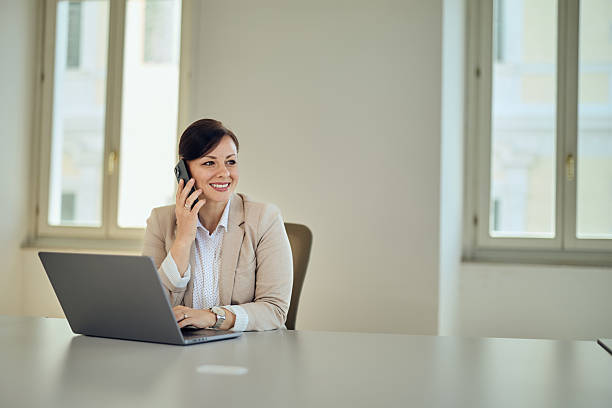 istock Professional Businesswoman Speaking On a Phone While Using Her Laptop in Office 2236893675