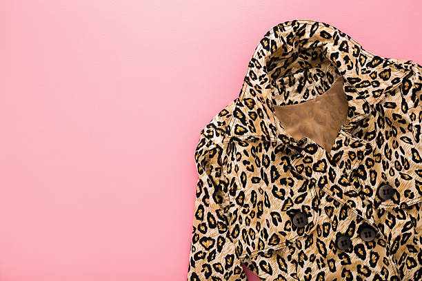 New soft leopard spot pattern coat on light pink table background. Pastel color. Closeup. Female elegant clothes. Empty place for text. Top down view.
