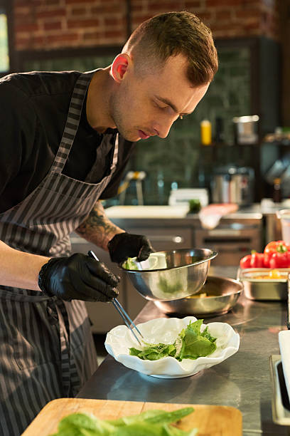 istock Young Adult Caucasian Man Assembling Fresh Green Salad in Restaurant Kitchen 2236902559