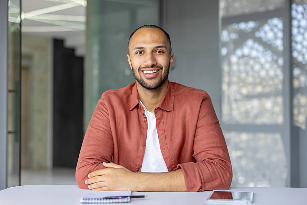 istock A handsome man smiles, sitting confidently in a well-lit office setting, looking pleased. 2236902878