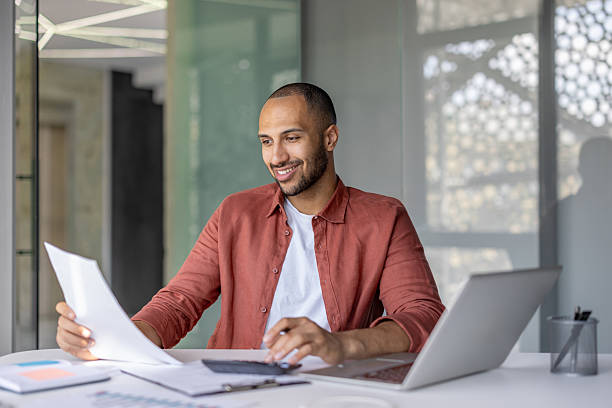 istock A man reviews documents and uses a calculator at his desk in a modern office, smiling. 2236902911