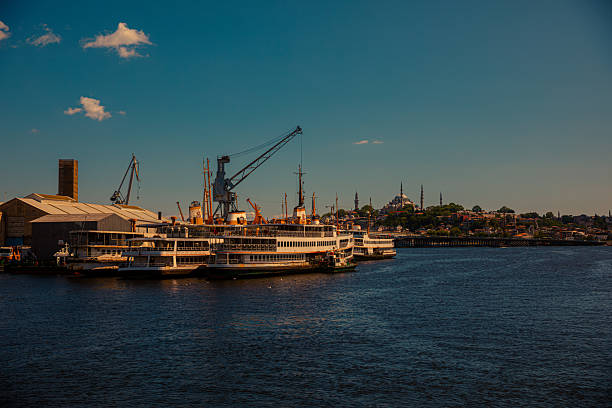 Ferries are docked at the shipyard along the Golden Horn in Istanbul, with industrial cranes on one side and the historic skyline of mosques visible in the background. The scene captures the city’s dual character, balancing maritime activity and centuries-old cultural heritage. This image reflects themes of transportation, urban life, and the symbolic connection between the Bosphorus and Istanbul’s identity.