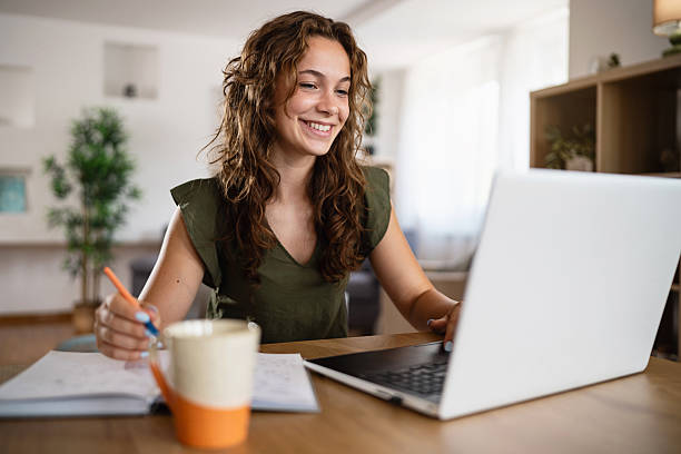 istock Young woman writing in notebook while working on laptop at dining table 2236905768