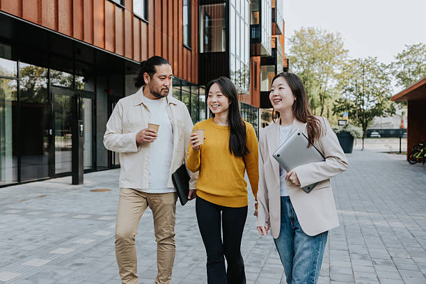 istock Three professionals walk outdoors with coffee and laptop, sharing a friendly business conversation in a modern city setting 2236909216