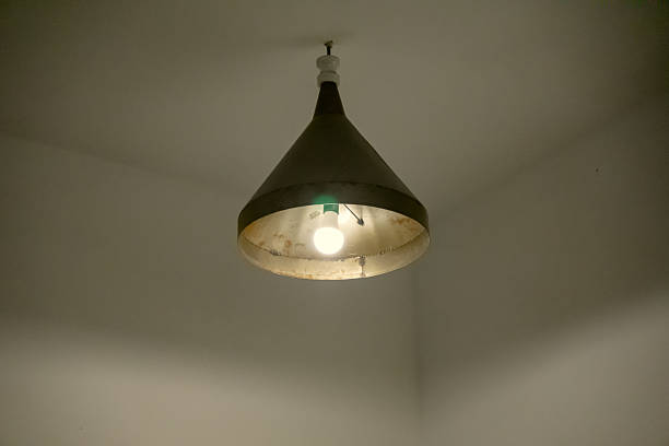 istock A single light bulb glowing inside an old, cone-shaped metal lampshade with visible rust and wear 2236917378