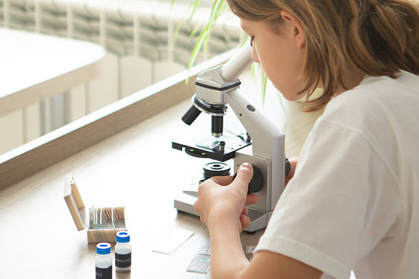 Girl studies biology at home through a microscope, embracing online learning in preparation for school year