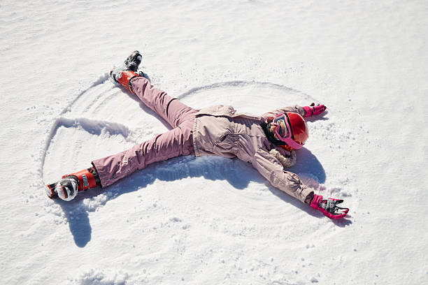 Winter portrait of a beautiful girl laughing and having a lot of fun in snow. She is making snow angel.