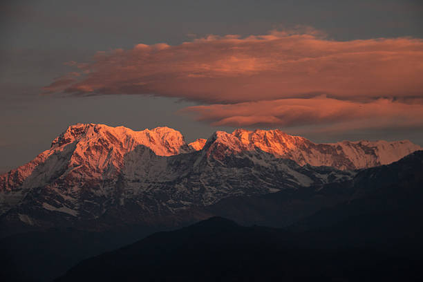 The first rays of sunrise bathe the Annapurna peaks in golden-red hues, turning the snow-capped mountains into a fiery spectacle. Clouds drift across the morning sky, enhancing the dramatic beauty of this Himalayan scene. The glowing peaks symbolize renewal, hope, and the timeless magnificence of Nepal’s natural wonders, attracting travelers and dreamers from around the globe to witness this breathtaking sunrise.
