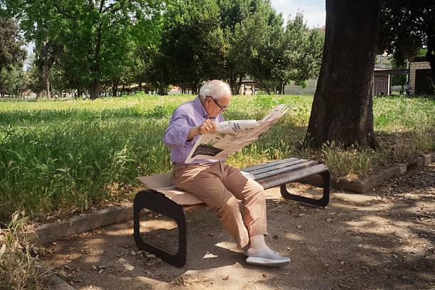 Aversa, Province of Caserta, April 2024. An elderly man sits on a park bench, intently reading the newspaper. A daily gesture that is becoming increasingly rare these days, replaced by phones and digital devices. The scene conveys tranquility, routine, and reflection, immersed in the urban greenery.