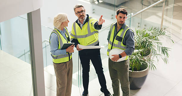 Civil engineer, pointing and people with blueprint in office, talk or plan for property development. Colleagues, woman and men with document for architecture, above and discussion for renovation