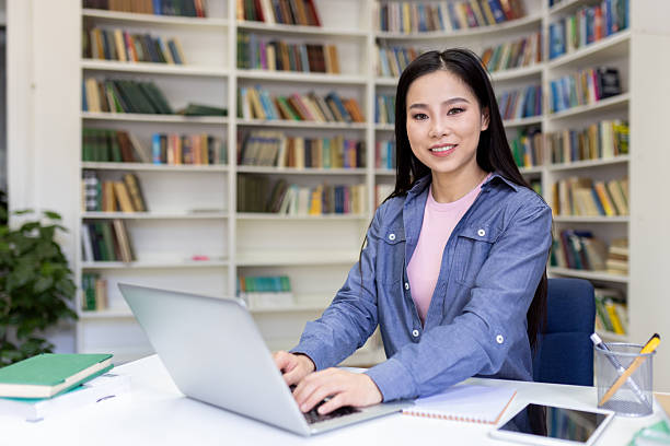 istock Attractive Asian woman smiles while working on her laptop at a library table. 2236931762