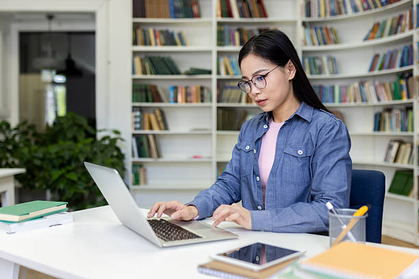 istock A student sits at a table in a library, using a laptop and surrounded by books. 2236931772
