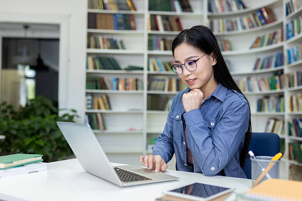 istock Focused young woman working on laptop amidst books in a library setting 2236931783