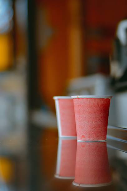 Two red paper cups placed on a reflective glass counter at a local beverage shop, creating a cozy and vibrant ambiance with a warm, blurred background with shallow depth of field